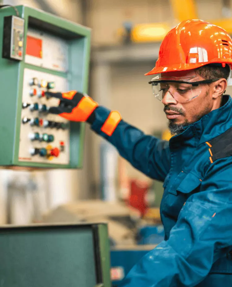 Vorlage_Hochkant Eine Person im Blaumann mit roten Schutzhelm an einer Maschine. Foto: Canva